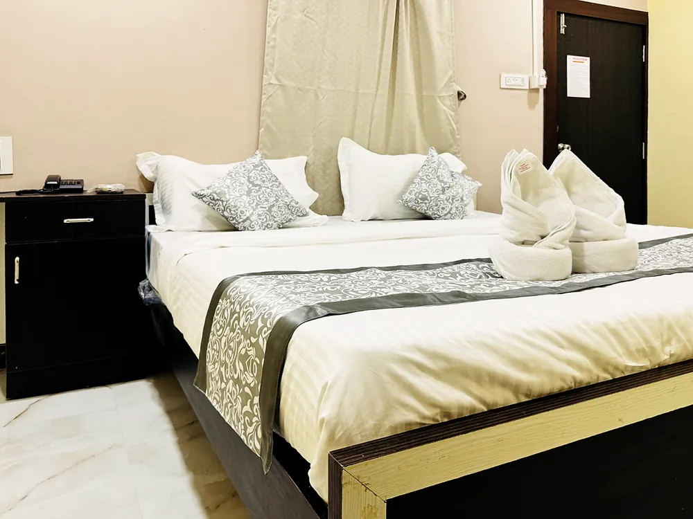 Guest room with folded towels on the bed and a bedside cabinet at Hotel Hyderabad Pulse